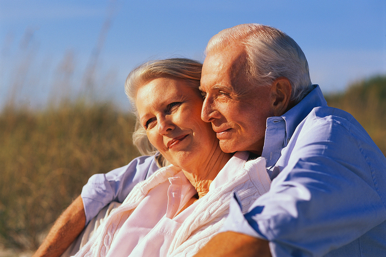 Senior couple sitting on front porch of their home. This image represents the target audience of reverse mortgages, which are people 62 and older.